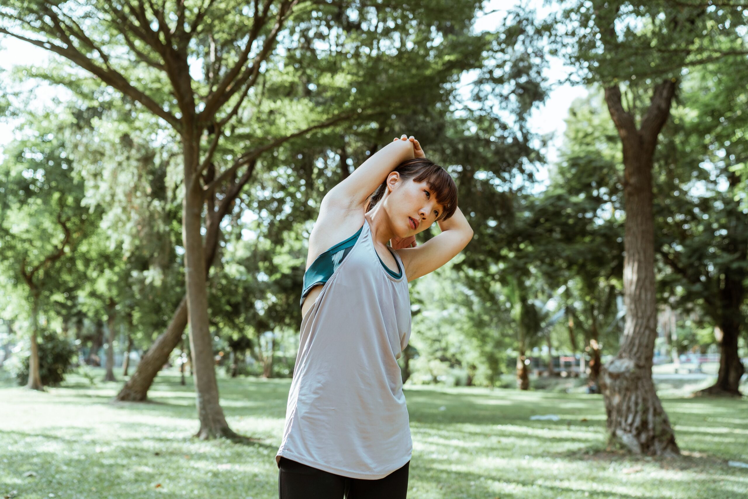 Woman stretching in a park wearing sleeveless top and leggings.